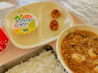 ピンクのトレーに給食が左から時計回りに牛乳、ラフランスゼリー、揚げしゅうまい、ごぼう入りマーボー豆腐、ごはんが並んでいる写真