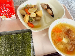 ピンクのトレーに給食が左から時計回りに牛乳、筑前煮、ぶりの照り焼き、油ふのみそ汁、味つけのりがのったごはんが並んでいる写真