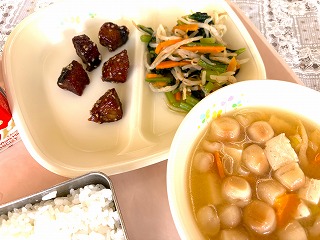 ピンクのトレーに給食が左から時計回りに牛乳、かつおのごまがらめ、小松菜のおひたし、豆ふのみそ汁、ごはんと並んでいる写真