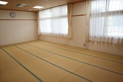 清潔な畳が敷き詰められ、白いカーテンがかかった窓と壁に掛けられた時計がある和室の写真