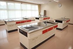 白を基調とし、赤い扉のシンクとコンロが設置された調理台がいくつか並んだ、清潔感のある公民館の調理室の写真