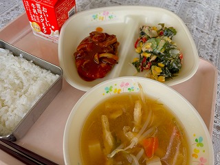 ピンクのトレーに給食が左から時計回りに牛乳、豆腐ハンバーグきのこソース、ツナとわかめのサラダ、油揚げのみそ汁、ごはんと並んでいる写真