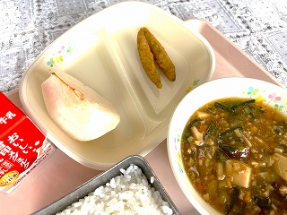 ピンクのトレーに給食が左から時計回りに牛乳、蔵王のなし、きびなごの天ぷら、なす入りマーボー豆腐、ごはんと並んでいる写真