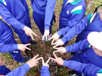 ジャージ姿の9名の生徒たちが右手でピースをしその指を隣の人とくっつけて形を作っているところをアップで写した写真