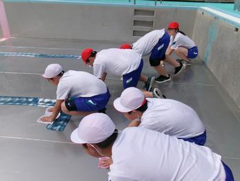 プールの端に並んだ体操着姿の6人の生徒たちが、一斉にプールの底の雑巾がけをしている様子の写真