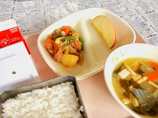 ピンクのトレーに給食が左から時計回りに牛乳、納豆、油ふじゃが、りんご、白菜のみそ汁、ごはんが並んでいる写真