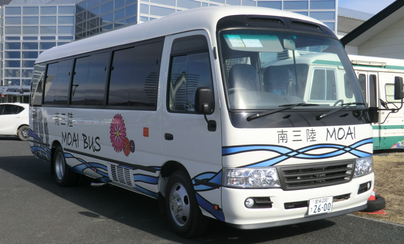 白地に青と黒の波模様と花のイラストが描かれ、車体の側面に「南三陸 MOAI BUS」と書かれているモアイバスの写真