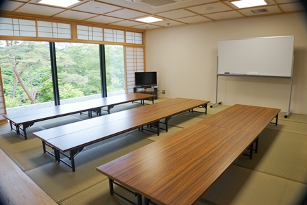 大きな窓には障子があり畳が敷かれた和室に長机が3列に置かれホワイトボードやテレビが設置された和室の写真