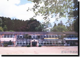 2階建ての木造の校舎が木立の中に建つ昔の学校の写真