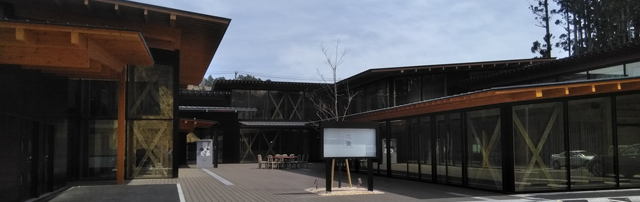 現代的なデザインで木材と調和した建物で、広い中庭にはテーブルと椅子が置かれ、ガラス張りの壁面が特徴的な図書館の写真