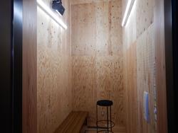 木製の壁に囲まれた狭い部屋で、左側に長い木製ベンチが設置され中央には黒いスツールが置かれた映像・音楽室Aの写真