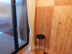 木製の壁と床に囲まれた部屋の隅に、白いカーテンがかかったガラスの引き戸があり、その前に黒い丸椅子が一脚置かれている映像・音楽室Bの写真