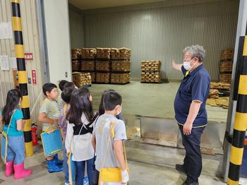 男性が右手で倉庫の中を指差し、児童たちが説明を聞いている町たんけんの写真