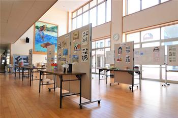 大きな窓から光が差し込む広い廊下に、たくさんの絵や書道作品が展示されている写真