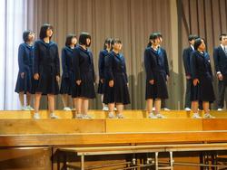 舞台の端に設置された2段のひな壇の上に制服姿の生徒たちが並び合唱をしている写真