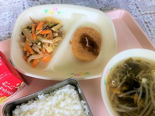 ピンクのトレーに給食が左から時計回りに牛乳、豚肉とたけのこのオイスター炒め、蔵王産さといもコロッケ(パックソース)、わかめスープ、ごはんが並べられている写真