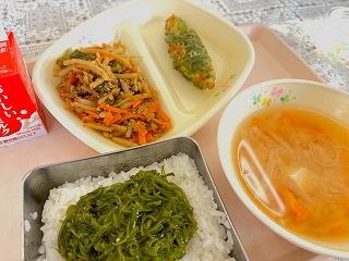 ピンクのトレーに給食が左から時計回りに牛乳、きんぴらごぼう、ささかまの磯部揚げ、ひきな汁、めかぶとろろがのったごはんが並んでいる写真