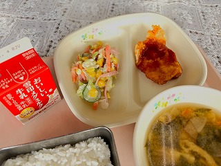 ピンクのトレーに給食が左から時計回りに牛乳、 コールスローサラダ、チキン南蛮、わかめのみそ汁、ごはんと並んでいる写真