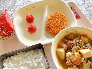 ピンクのトレーに給食が左から時計回りに牛乳、いちご、ポテトコロッケ、パックソース、すき焼き煮、ごはんが並んでいる写真
