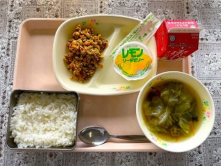 ピンクのトレーに給食が左から時計回りに夏野菜のガパオライスの具、レモンソーダゼリー、 牛乳、おくらとわかめのスープ、ごはんと並んでいる写真