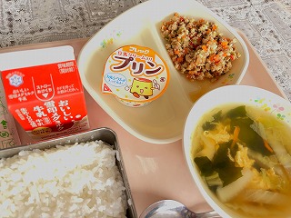ピンクのトレーに給食が左から時計回りに牛乳、豆乳プリン、ガパオライスの具、わかめと玉子のスープ、ごはんが並んでいる写真