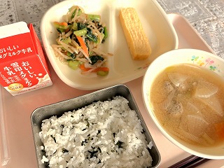 ピンクのトレーに給食が左から時計回りに牛乳、小松菜のおひたし、厚焼きたまご、さんまのつみれ汁、わかめごはんが並んでいる写真