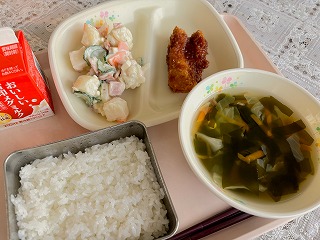 ピンクのトレーに給食が左から時計回りに牛乳、 マセドアンサラダ、手作りチキンカツ、キャベツとわかめのスープ、ごはんと並んでいる写真