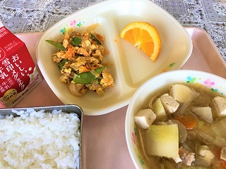 ピンクのトレーに給食が左から時計回りに牛乳、油ふ丼の具、オレンジ、豚汁、ごはんが並んでいる写真