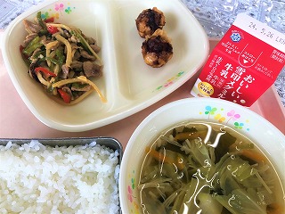 ピンクのトレーに給食が左から時計回りにチンジャオロースー、あげしゅうまい、牛乳、わかめと春雨のスープ、ごはんが並べられている写真