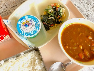 ピンクのトレーに給食が左から時計回りに牛乳、ヨーグルト、わかめと大根のサラダ、ポークカレー、ごはんが並んでいる写真