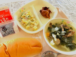 ピンクのトレーに給食が左から時計回りに牛乳、さつまいものサラダ、鶏肉のバーベキューソース、ケールとかぶのコンソメスープ、ソフトパンが並んでいる写真