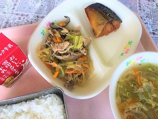 ピンクのトレーに給食が左から時計回りに牛乳、たっぷり野菜のチャプチェ、さばのヤンニョム風、卵とレタスのスープ、ごはんが並べられている写真