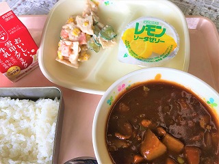 ピンクのトレーに給食が左から時計回りに牛乳、れんこんサラダ、レモンソーダゼリー、ハヤシライス、ごはんが並んでいる写真