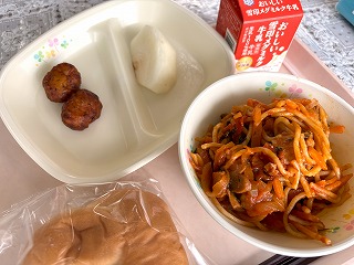 ピンクのトレーに給食が左から時計回りにレモンバジルナゲット、蔵王のなし、牛乳、夏野菜とケールのトマトスパゲティー、ミルクパンと並んでいる写真