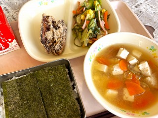 ピンクのトレーに給食が左から時計回りに牛乳、さば竜田揚げ、りっちゃんサラダ、油ふのみそ汁、味つけのりがのったごはんが並んでいる写真