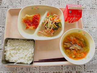 ピンクのトレーに給食が左から時計回りにヤンニョムチキン、もやしのナムル、牛乳、春雨スープ、ごはんが並んでいる写真