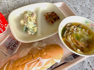 ピンクのトレーに給食が左から時計回りに牛乳、さつまいもサラダ、鶏肉のマーマレード焼き、ワンタンスープ、ソフトパン、いちごジャムと並んでいる写真