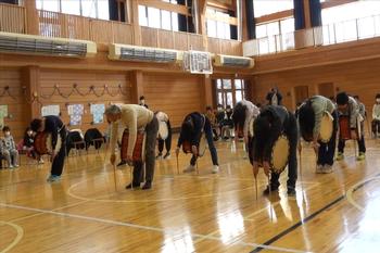 村岡さんと同じく子どもたちが胸にかけた太鼓に体を覆いかぶせるように前かがみの姿勢をとって、両手には細長いバチを持ち、バチ先を体育館の床にまっすぐ下ろしてつけている様子の写真
