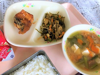 ピンクのトレーに給食が左から時計回りに牛乳とミニゼリー、さばから揚げおろしソース、すき昆布の煮物、小松菜と油麩のみそ汁、ごはんが並んでいる写真