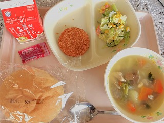 ピンクのトレーに給食が左から時計回りに牛乳、パックソース、ハムカツ、コールスローサラダ、冬野菜のポトフ、丸パンが並んでいる写真