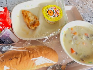 ピンクのトレーに給食が左から時計回りに牛乳、鶏肉のレモンソースがけ、いよかんゼリー、冬野菜のクリーム煮、コッペパン、ブルーベリージャムが並んでいる写真