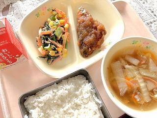 ピンクのトレーに給食が左から時計回りに牛乳、小松菜とにんじんのごまマヨサラダ、さばのから揚げりんごソース、油ふ入りはっと汁、ごはんが並んでいる写真