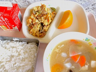 ピンクのトレーに給食が左から時計回りに牛乳、油ふ丼の具、オレンジ、みそけんちん汁、ごはんが並んでいる写真
