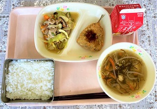 ピンクのトレーに給食が左から時計回りに野菜炒め、あじフライ（パックソース）、牛乳、もずくのスープ、ごはんが並んでいる写真