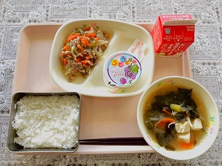 ピンクのトレーに給食が左から時計回りにねぎ塩豚丼の具、ぶどうゼリー、牛乳、わかめと豆腐のみそ汁、ごはんが並んでいる写真