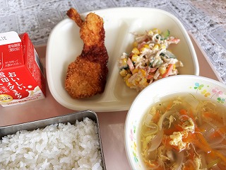 ピンクのトレーに給食が左から時計回りに牛乳、手作りチキンカツ、切干大根のかみかみサラダ、たまごスープ、ごはんが並んでいる写真