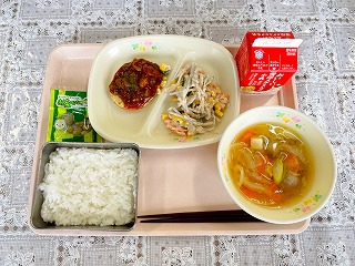 ピンクのトレーに給食が左から時計回りに抹茶豆、豆腐ハンバーグきのこソース、ごぼうサラダ、牛乳、いわしのつみれ汁、ごはんが並んでいる写真