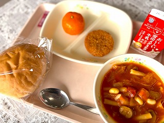 ピンクのトレーに給食が左から時計回りにハムカツソース、冷凍みかん、ハムカツサンド、牛乳、ミネストローネ、丸パンと並んでいる写真