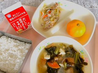 ピンクのトレーに給食が左から時計回りに牛乳、ねぎ塩豚丼の具、みかん、わかめと油ふのみそ汁、ごはんが並んでいる写真