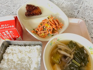 ピンクのトレーに給食が左から時計回りに牛乳、ふか肉のゆかり揚げ、人参のごまドレサラダ、しめじと小松菜のみそ汁、ごはんと並んでいる写真